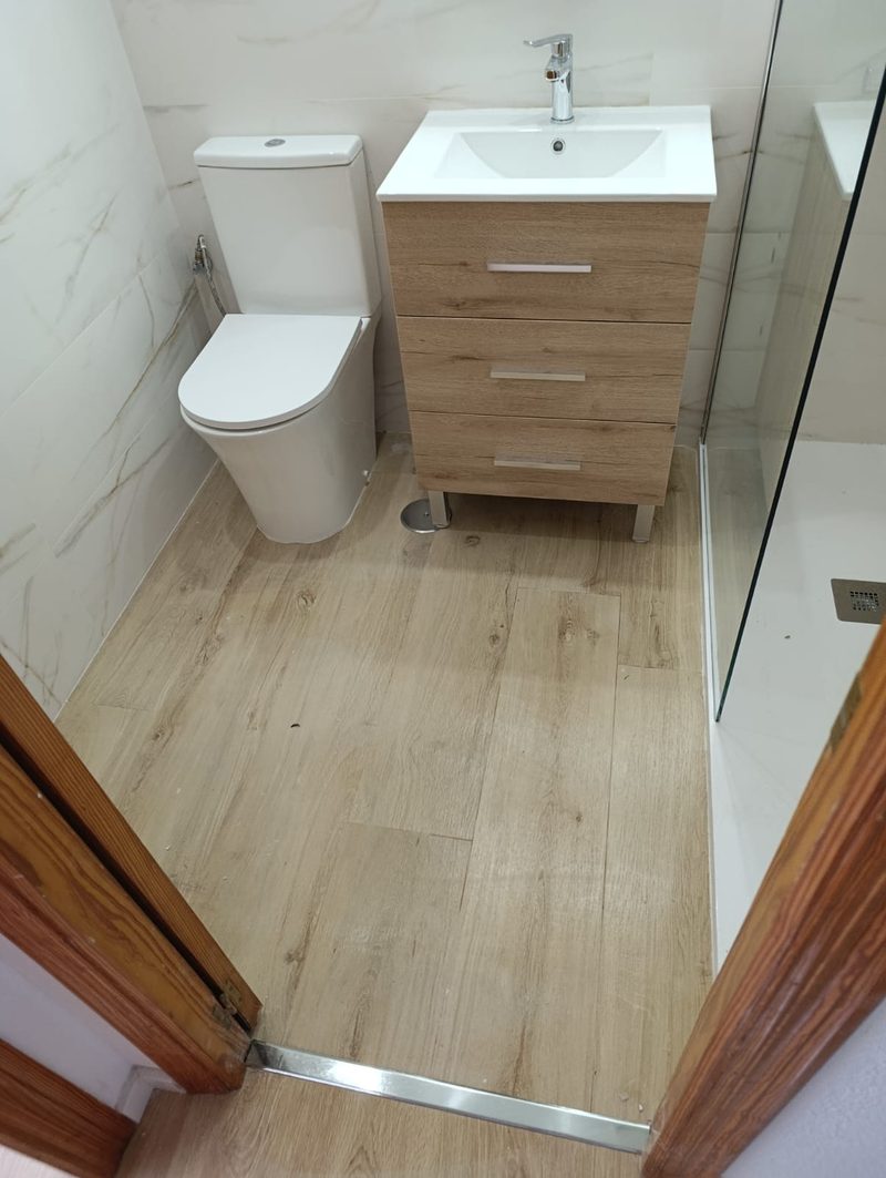 Reforma de baño en la Albufereta (Alicante): mueble de lavabo de madera clara, alicatado imitación mármol y suelo porcelánico tipo tarima